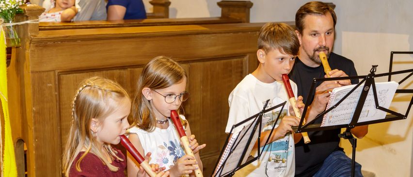Ein Mann und drei Kinder spielen Blockflöten in einer Kirche, mit Musikblättern vor ihnen.