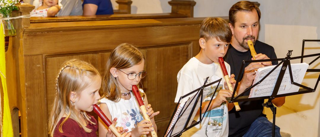 Ein Mann und drei Kinder spielen Blockflöten in einer Kirche, mit Musikblättern vor ihnen.