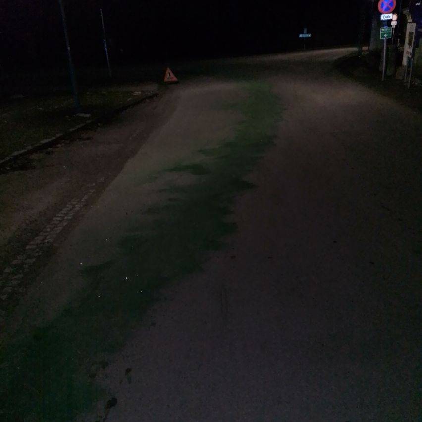 Eine dunkle Nacht mit einer nassen Straße. Es gibt ein kleines dreieckiges Schild am Straßenrand, das auf eine potenzielle Gefahr hinweist.