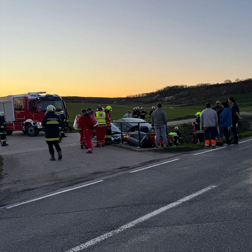 Rettungskräfte sind am Unfallort, mit Feuerwehrwagen und Schaulustigen am Straßenrand.