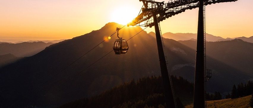 Eine Seilbahn fährt bei Sonnenuntergang einen Berghang hinauf, mit leuchtenden Farben, die den Himmel bemalen.
