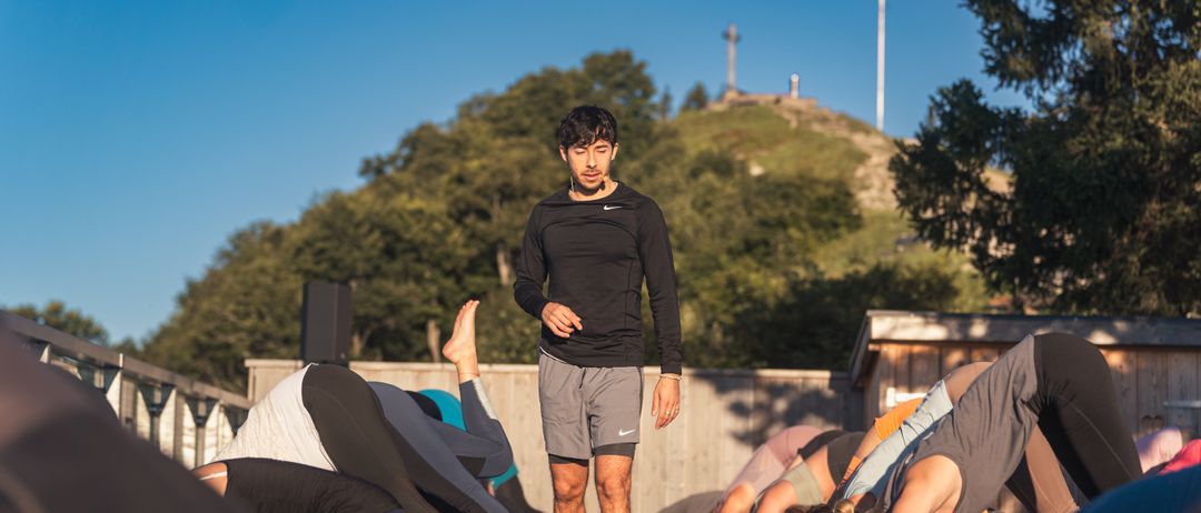 Ein Mann leitet eine Yoga-Sitzung an einem sonnigen Tag, wobei die Teilnehmer in verschiedenen Yoga-Posen auf dem Boden liegen.
