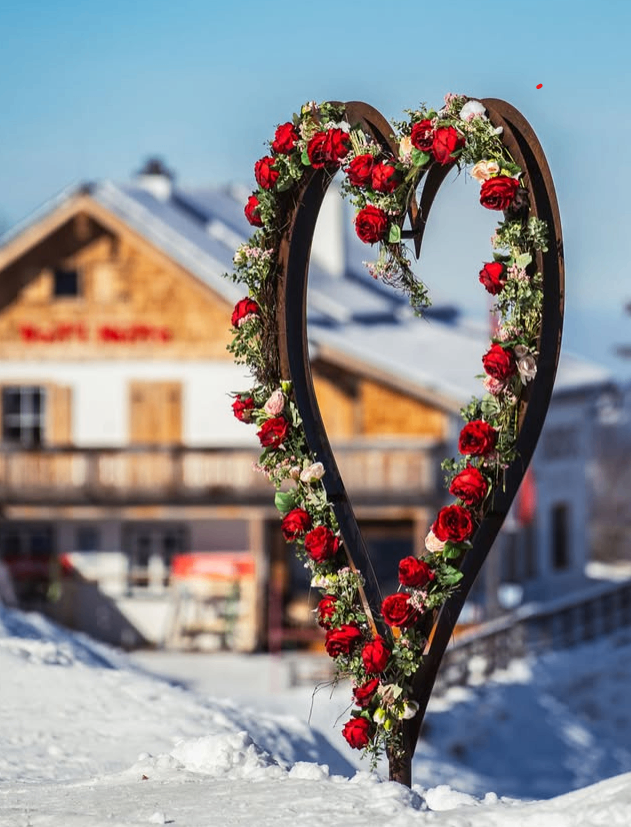 Ein herzförmiger Rosenkranz steht im Schnee vor einem Haus.