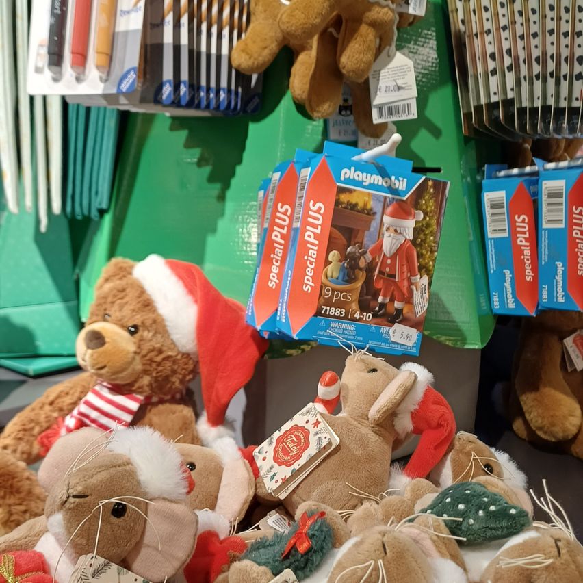 A display of Christmas-themed plush toys, including Santa Claus and reindeer, with a special plus pack price tag hanging above.