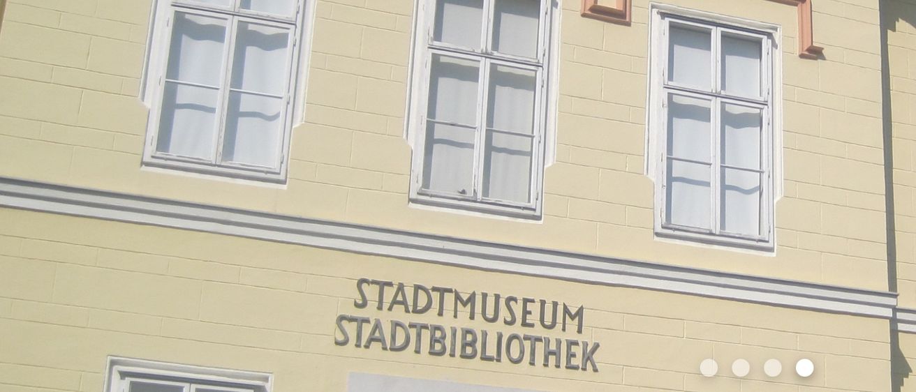 Ein Gebäude mit gelber Wand hat zwei Fenster. Unter den Fenstern befindet sich ein Schild, das Stadtmuseum Stadtbibliothek besagt.