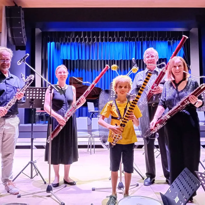 Eine Gruppe von Musikern steht in einer Reihe auf einer Bühne mit Musikinstrumenten. Sie scheinen ein Konzert aufzuführen oder sich darauf vorzubereiten.