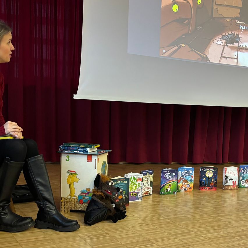 Eine Frau sitzt vor einer Projektionsleinwand und schaut sich einen Zeichentrickfilm an. Bücher sind in einer Reihe auf dem Boden angeordnet.