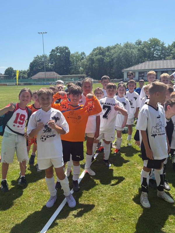 Eine Gruppe junger Fußballspieler steht auf dem Feld, trägt verschiedene Teamtrikots und lächelt für die Kamera.