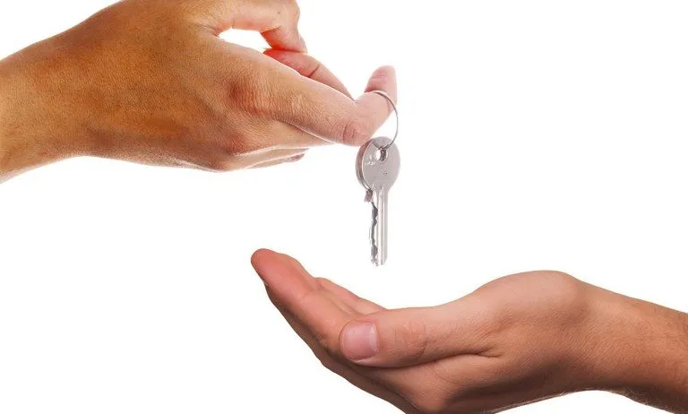 Eine Hand hält einen Schlüssel und reicht ihn einer anderen Hand. Der Schlüssel ist an einem Schlüsselbund befestigt.