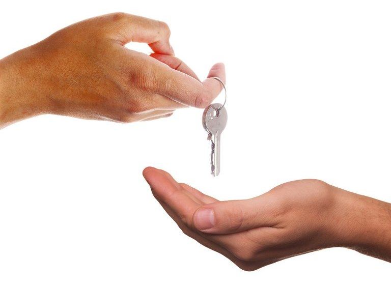 Eine Hand hält einen Schlüssel und reicht ihn einer anderen Hand. Der Schlüssel ist an einem Schlüsselbund befestigt.