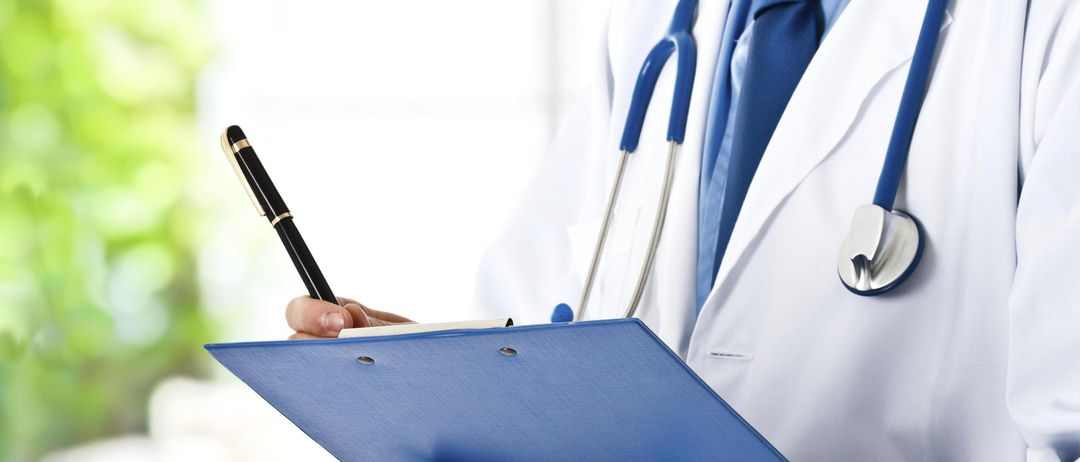 Ein Arzt in einem weißen Kittel hält eine blaue Mappe und einen Stift in den Händen.