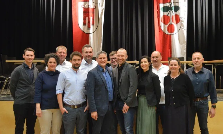 Eine Gruppe von Menschen posiert für ein Foto vor einer Bühne mit zwei Fahnen im Hintergrund.