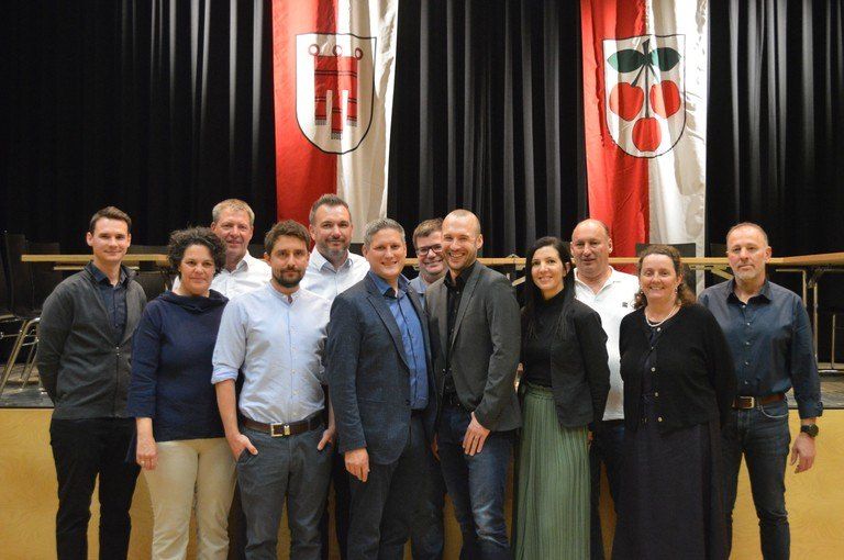 Eine Gruppe von Menschen posiert für ein Foto vor einer Bühne mit zwei Fahnen im Hintergrund.