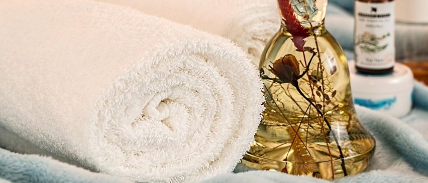 Zwei gerollte Handtücher und eine Flasche mit klarer Flüssigkeit und einer Blume darin auf einer blauen Decke.