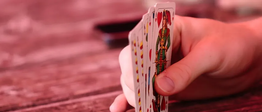 Eine Hand hält ein Kartenspiel mit einer rot gekleideten Figur auf einer von ihnen auf einem Holztisch.