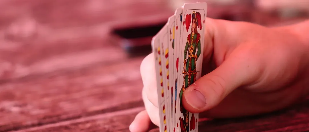 Eine Hand hält ein Kartenspiel mit einer rot gekleideten Figur auf einer von ihnen auf einem Holztisch.