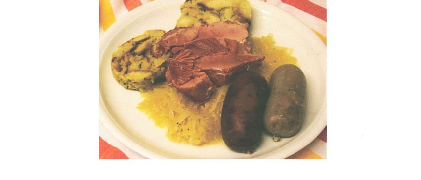 Ein Teller mit Fleisch, Kartoffeln und einer Wurst auf einem weißen Teller mit einem rot-gelb gestreiften Tuch. Das Bild enthält auch einen Textüberlagerung mit Veranstaltungsdetails.