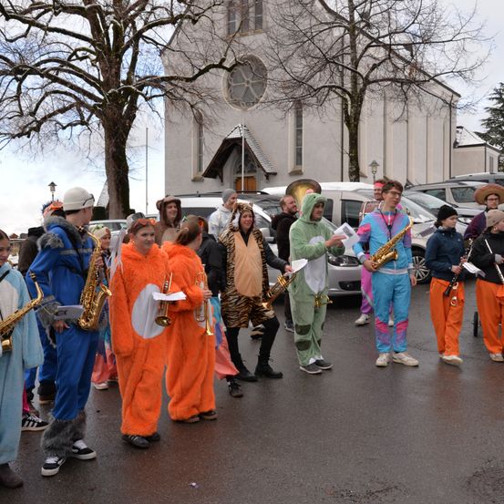 Eine Gruppe von Menschen in farbenfrohen Kostümen tritt vor einer Kirche auf und hält verschiedene Musikinstrumente in den Händen.