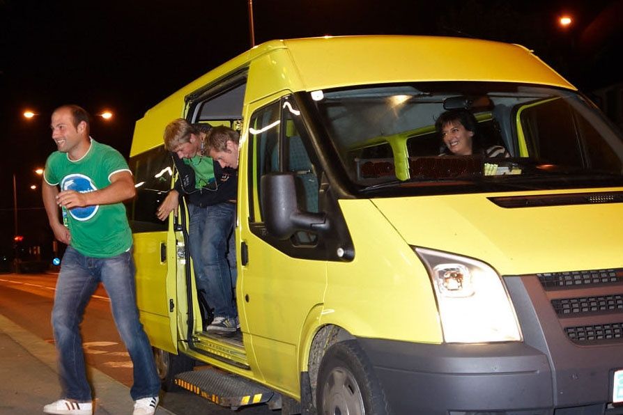 Ein Mann steigt in einen gelben Van ein, während ein anderer Mann die Tür offen hält. Eine Frau fährt den Van.