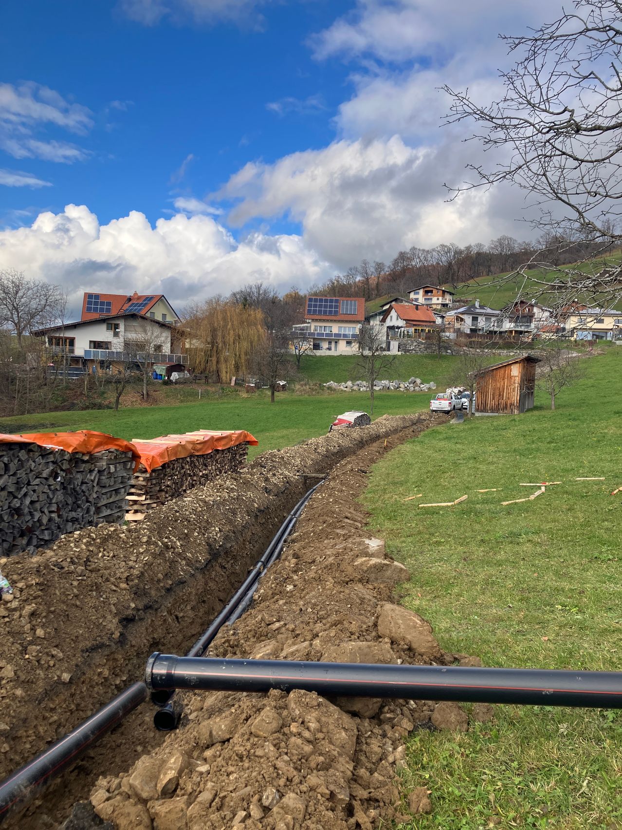 Ein offener Graben für die Verlegung von Rohrleitungen liegt in einem Grasfeld mit Häusern mit Solarmodulen im Hintergrund.