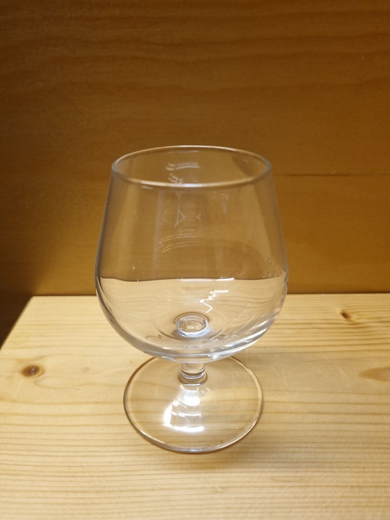 Ein leeres klares Weinglas steht auf einem holzfarbenen Tisch. Das Glas hat eine konische Schüssel und einen Stiel.