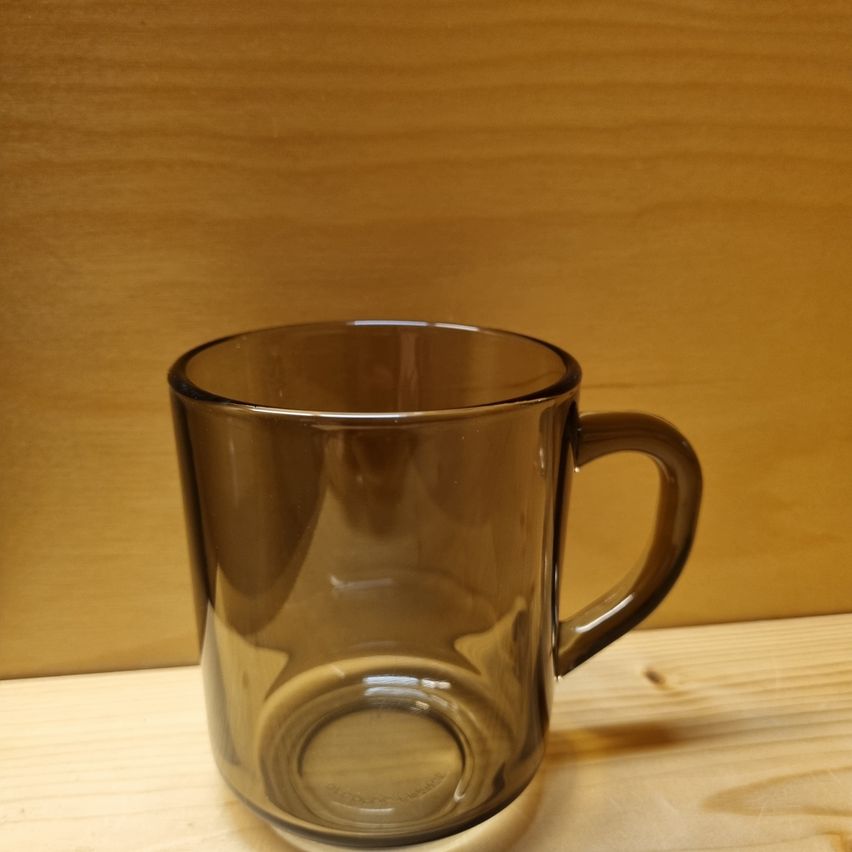 Ein leerer brauner Glasbecher mit Griff steht auf einer Holzoberfläche. Der Becher spiegelt den hölzernen Hintergrund.