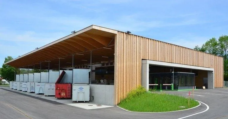 Ein modernes Gebäude mit Holzfassade, das eine lange Reihe weißer Container, einen roten Container am Ende und einen großen offenen Bereich aufweist.