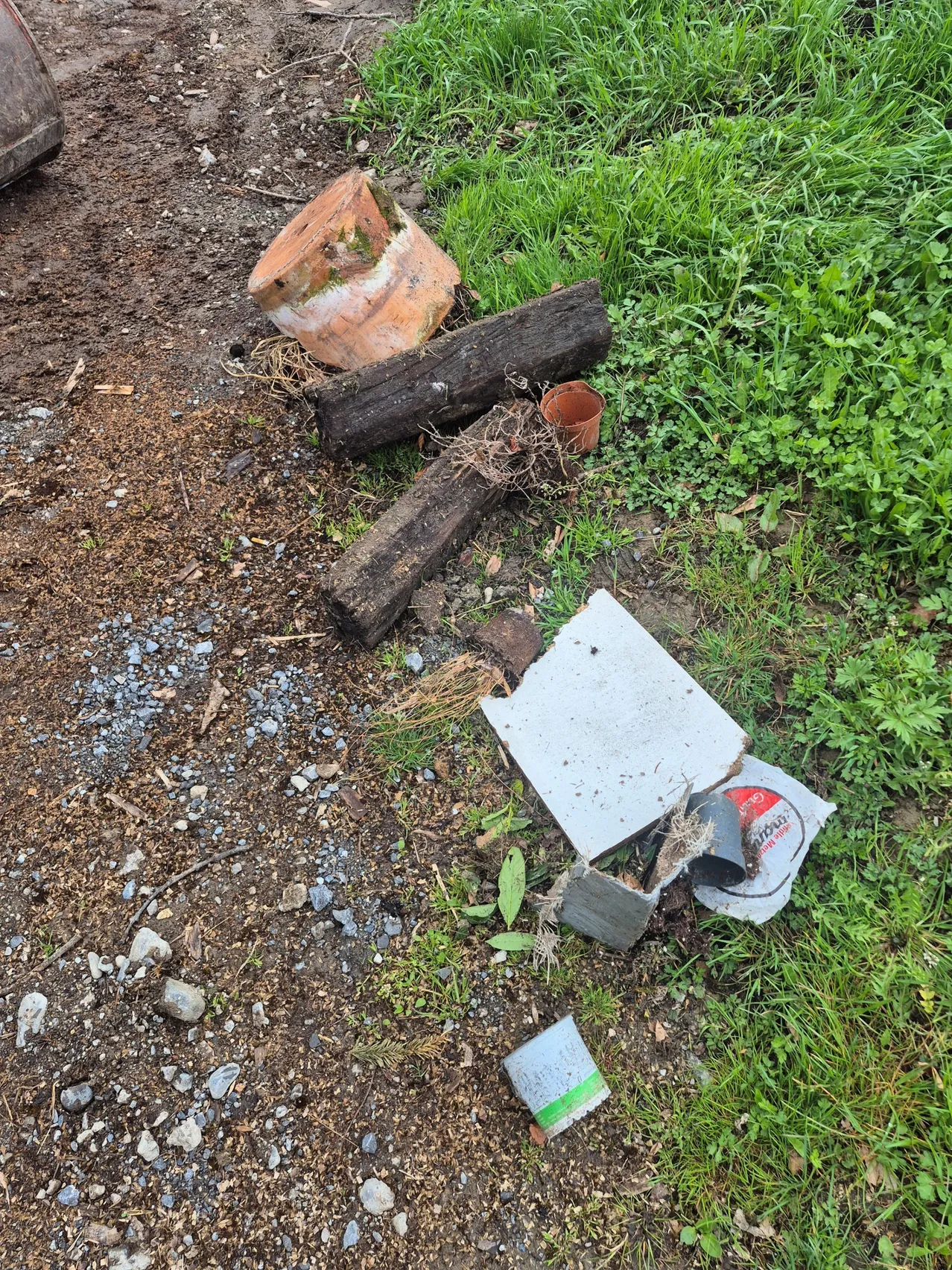 Ein verschmutztes Gebiet mit verstreuten zerbrochenen Töpfen, Holzstämmen und Müll. Ein zerrissenes Stück Metall und andere Gegenstände liegen auf dem Boden.