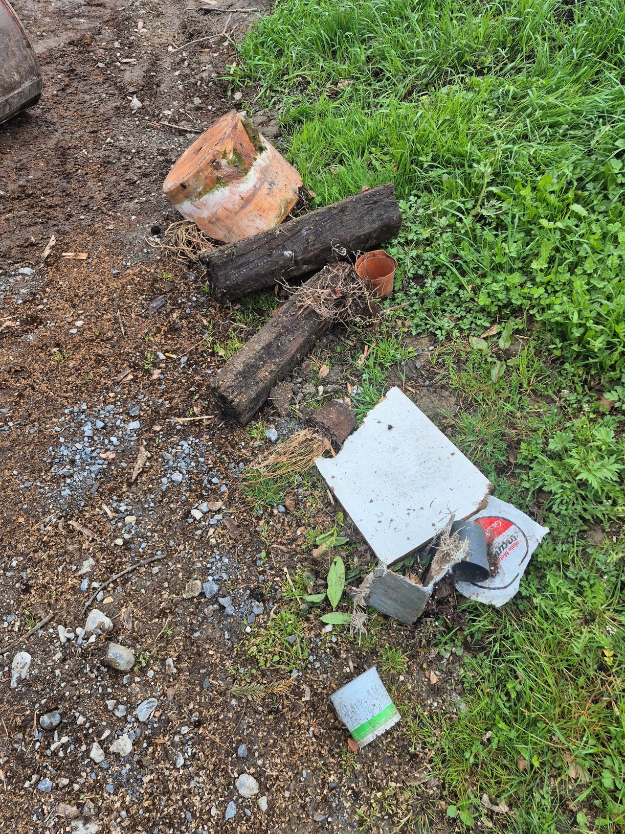 Ein verschmutztes Gebiet mit verstreuten zerbrochenen Töpfen, Holzstämmen und Müll. Ein zerrissenes Stück Metall und andere Gegenstände liegen auf dem Boden.