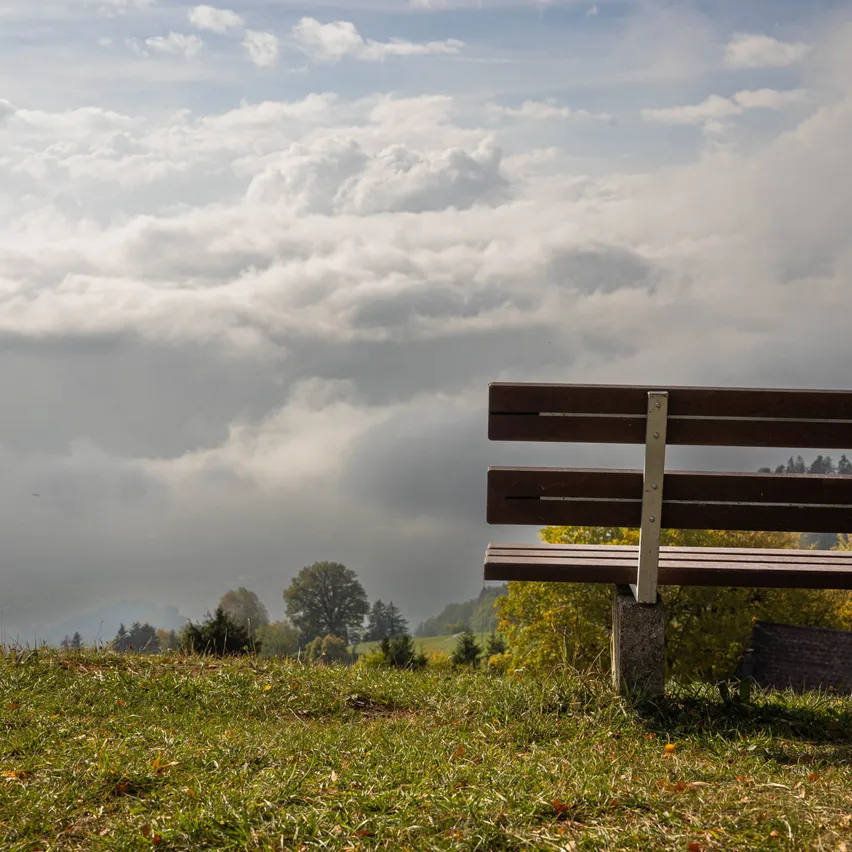 Eine Bank auf einem Grashügel unter einem bewölkten Himmel.