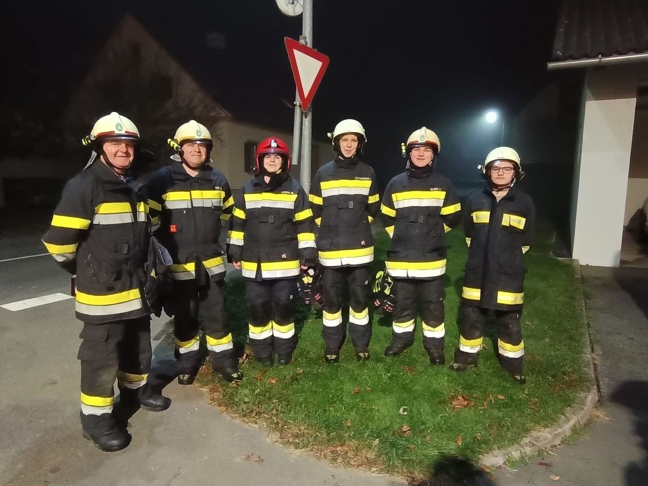 A group of firefighters wearing uniforms pose for a photo at night. There are five of them.