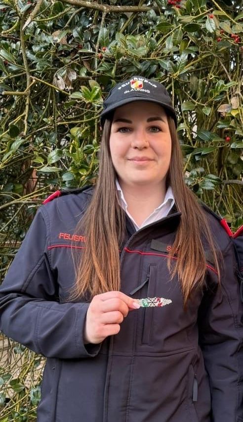 Eine Frau in einer schwarzen Uniform hält ein Armband vor einem Busch mit roten Beeren.