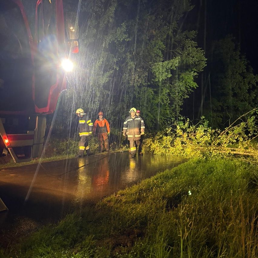 Firefighters are outside in the rain with a red fire truck. One has a red helmet, another has a yellow helmet.