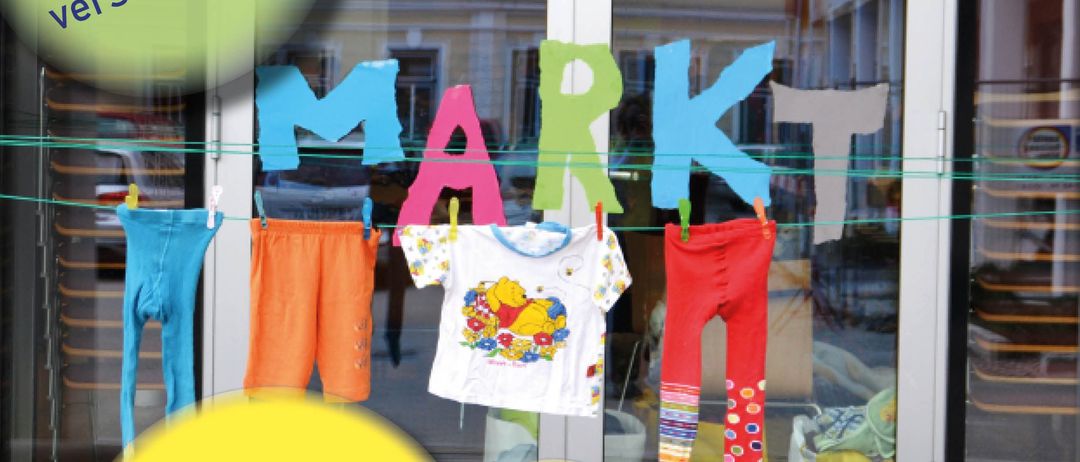 Plakat für einen Kleidermarkt mit bunten Buchstaben, die 'Floh Markt' lesen. Kleidung hängt an einer Wäscheleine. Daten und Zeiten sind aufgeführt, zusammen mit einem Ort, Rathaus Hermagor.