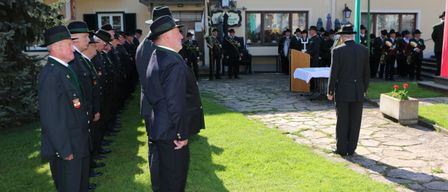 Eine Gruppe formell gekleideter Männer steht in einer Reihe auf einem Rasenbereich, möglicherweise für eine Zeremonie, vor einem Gebäude namens Gasthof Pension Grundl.