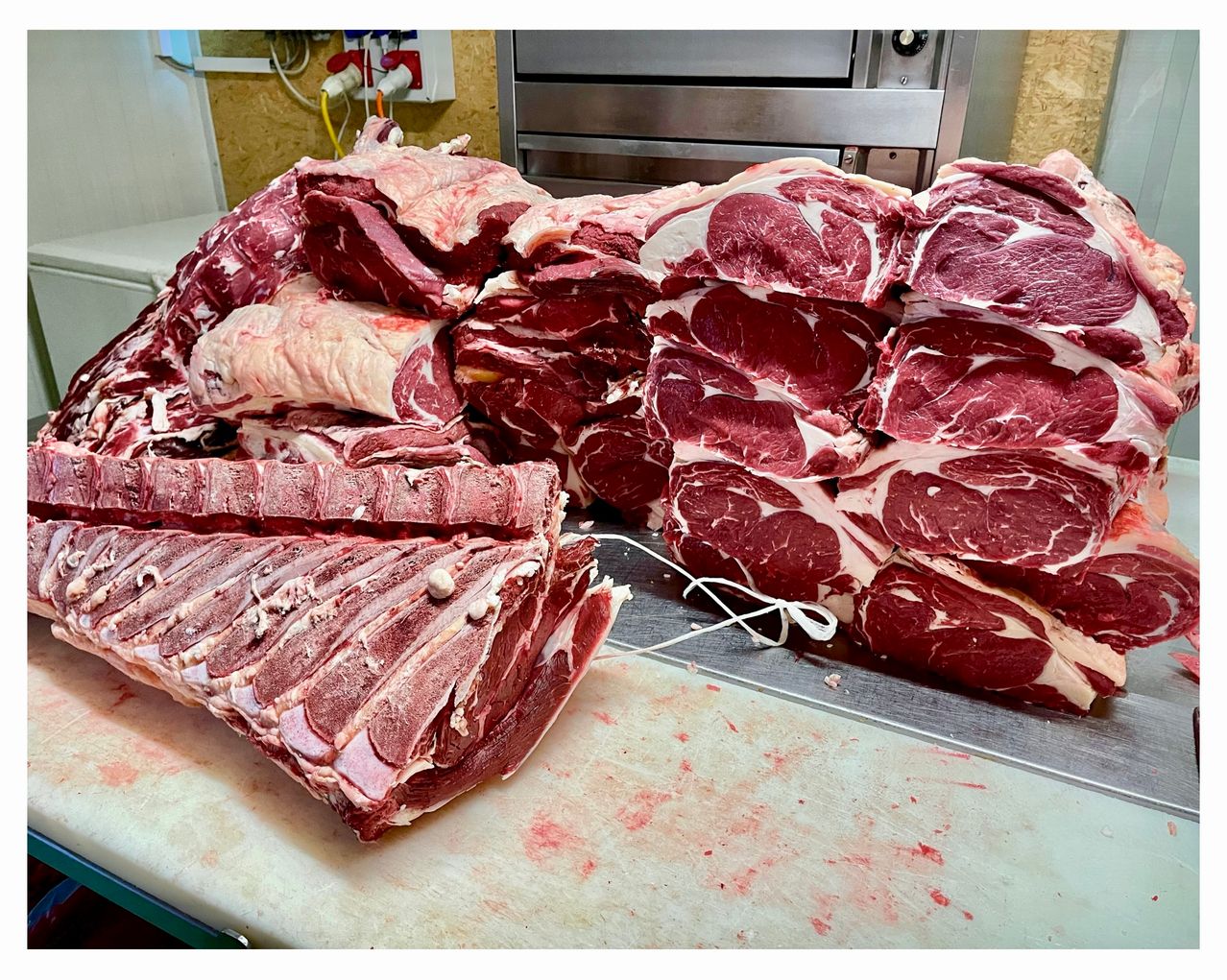 Ein Haufen frisches rotes Fleisch, wahrscheinlich Rindfleisch, wird auf einem weißen Schneidebrett mit einigen Blutflecken ausgestellt. Das Fleisch ist in Reihen angeordnet und scheint bereit zum Verkauf zu sein.