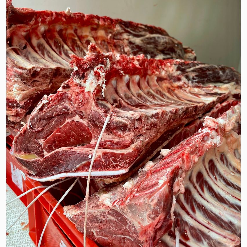 Ein Nahaufnahme von rohen Rinderrippen, ordentlich in einem roten Kasten gestapelt, mit sichtbaren Rippenknochen und Muskelfasern. Das Fleisch ist frisch und rot, was auf seine Qualität hinweist.