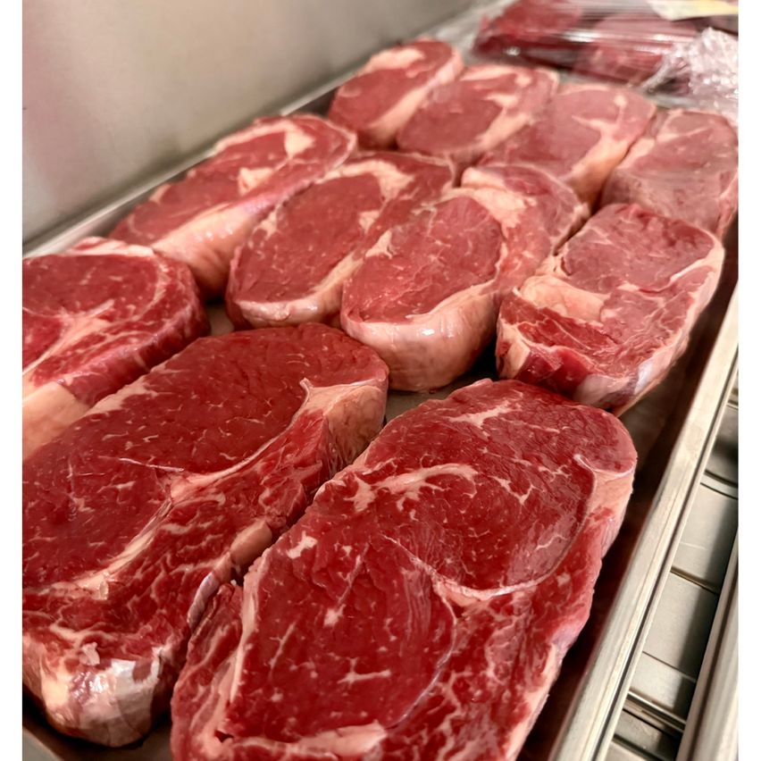 Eine Nahaufnahme von mehreren frischen rohen Rindersteaks, ordentlich auf einem Edelstahltablett angeordnet. Jedes Steak hat eine leuchtend rote Farbe und ist einzeln in Plastik eingewickelt.