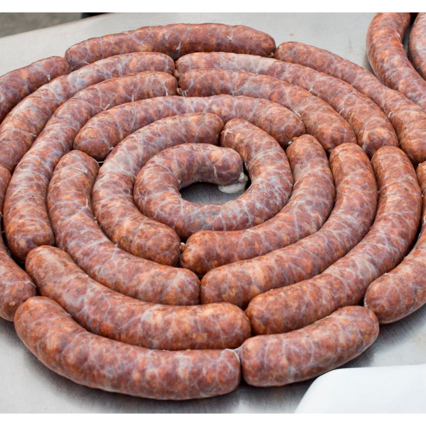 Eine kreisförmige Anordnung von braunen Würstchen wird auf einer metallischen Oberfläche präsentiert. Die Würste sind in Plastik eingewickelt und haben eine leichte Spiralform.