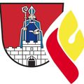 Ein Wappen zeigt einen Bischof mit Stab und Buch vor einer Burg auf rotem Hintergrund. Daneben ist ein Flammensymbol in Rot und Gelb.