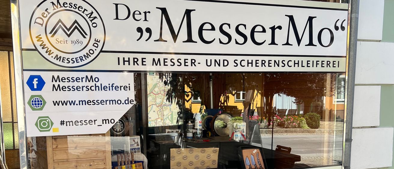 Schaufenster mit einem Schild 'Der MesserMo', das Messer, Beratung, Verkauf und Service anbietet. Im Inneren sind Gegenstände auf Regalen ausgestellt.