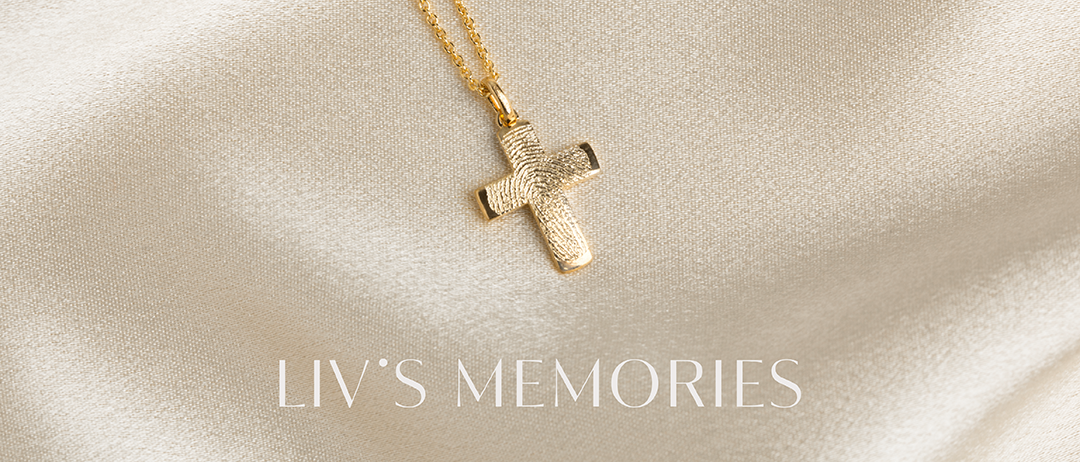 Zwei goldene Halsketten mit Kreuzanhängern liegen auf einem cremefarbenen Stoff. Eine hat einen strukturierten Kreuzanhänger. Unten steht der Markenname 'LIV'S MEMORIES'.