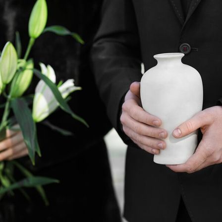Ein Mann und eine Frau in Schwarz halten eine weiße Vase mit einem Strauß aus grünen und weißen Blumen während einer feierlichen Veranstaltung.