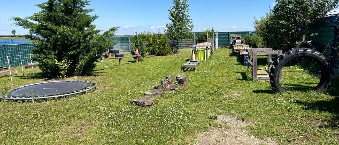 Ein Outdoor-Spielplatz mit Trampolin, Holzbänken und einer Reifen-Hindernisparcours an einem sonnigen Tag.