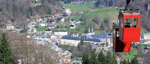 Luftaufnahme einer Stadt mit vielen Gebäuden und Bäumen. Eine rote Seilbahn ist sichtbar.