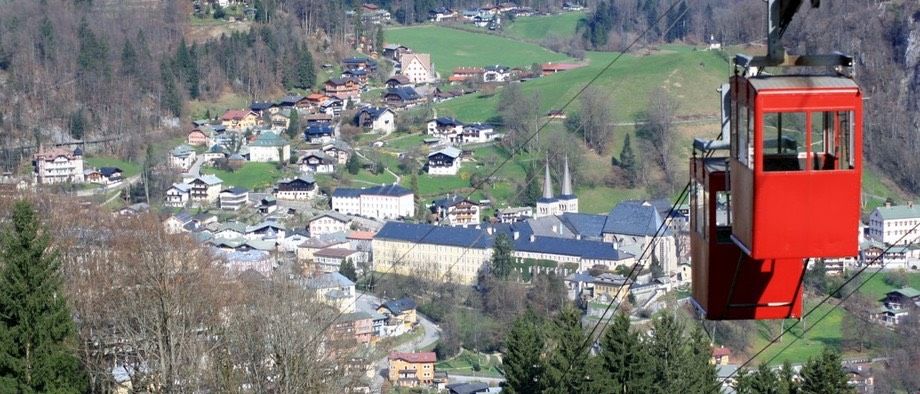 Luftaufnahme einer Stadt mit vielen Gebäuden und Bäumen. Eine rote Seilbahn ist sichtbar.