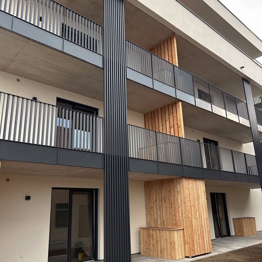 Ein modernes Apartmentgebäude mit Balkonen, Glastüren und Holzpaneelen. Balkone haben Metallgeländer.
