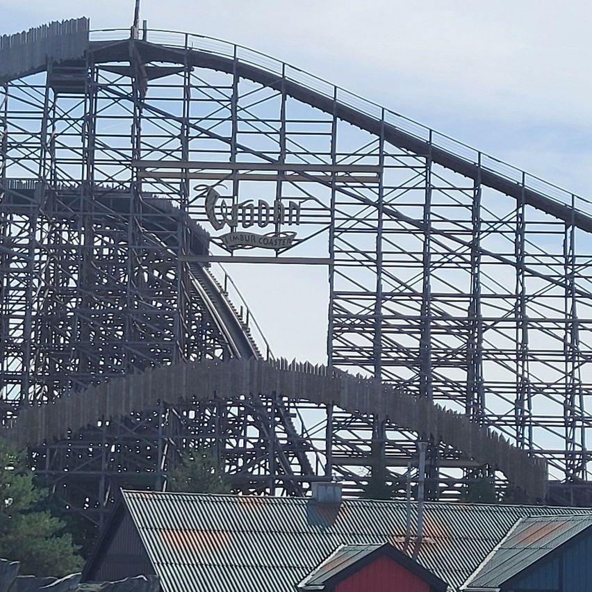 Eine große Holzachterbahn mit einem Schild, das oben 'Wood' steht. Die Achterbahn befindet sich im Bau mit sichtbaren Metallgerüsten.