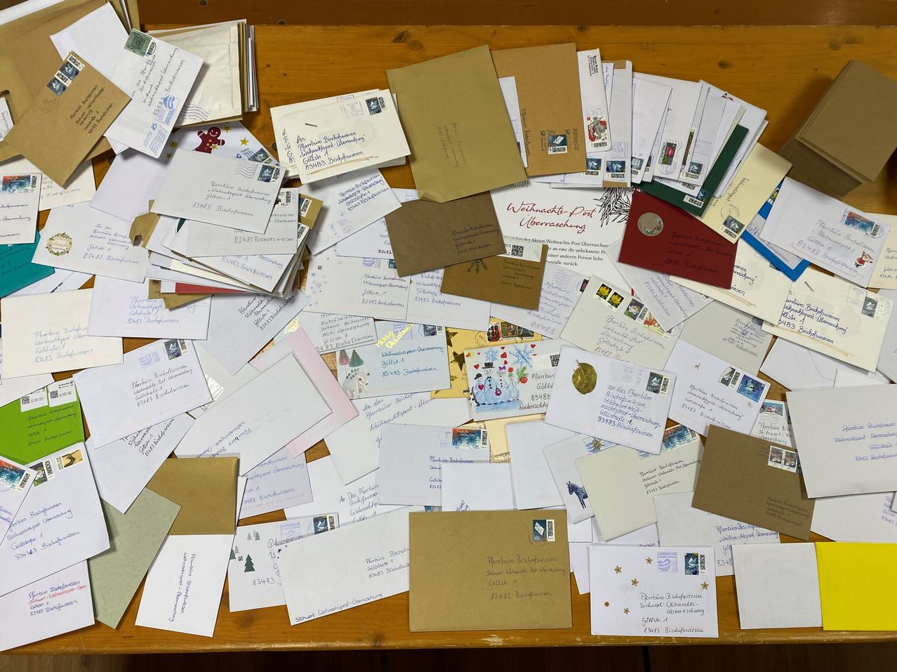 Ein hölzerner Tisch, bedeckt mit verschiedenen Weihnachtskarten und Briefen, einige mit Briefmarken und fremdsprachigem Text, in einem Haufen angeordnet.