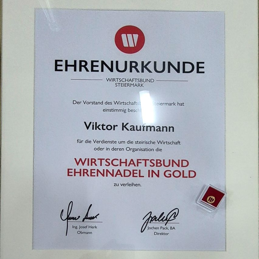 Ein Zertifikat, verliehen von der Steirischen Wirtschaftsbund, an Viktor Kaufmann für seine Beiträge zur steirischen Wirtschaft. Das Zertifikat zeigt eine goldene Medaille und ist unterzeichnet von Ing. Josef Herk, dem Vorstand des Wirtschaftsbundes, und Jochen Pack, BA, dem Direktor.